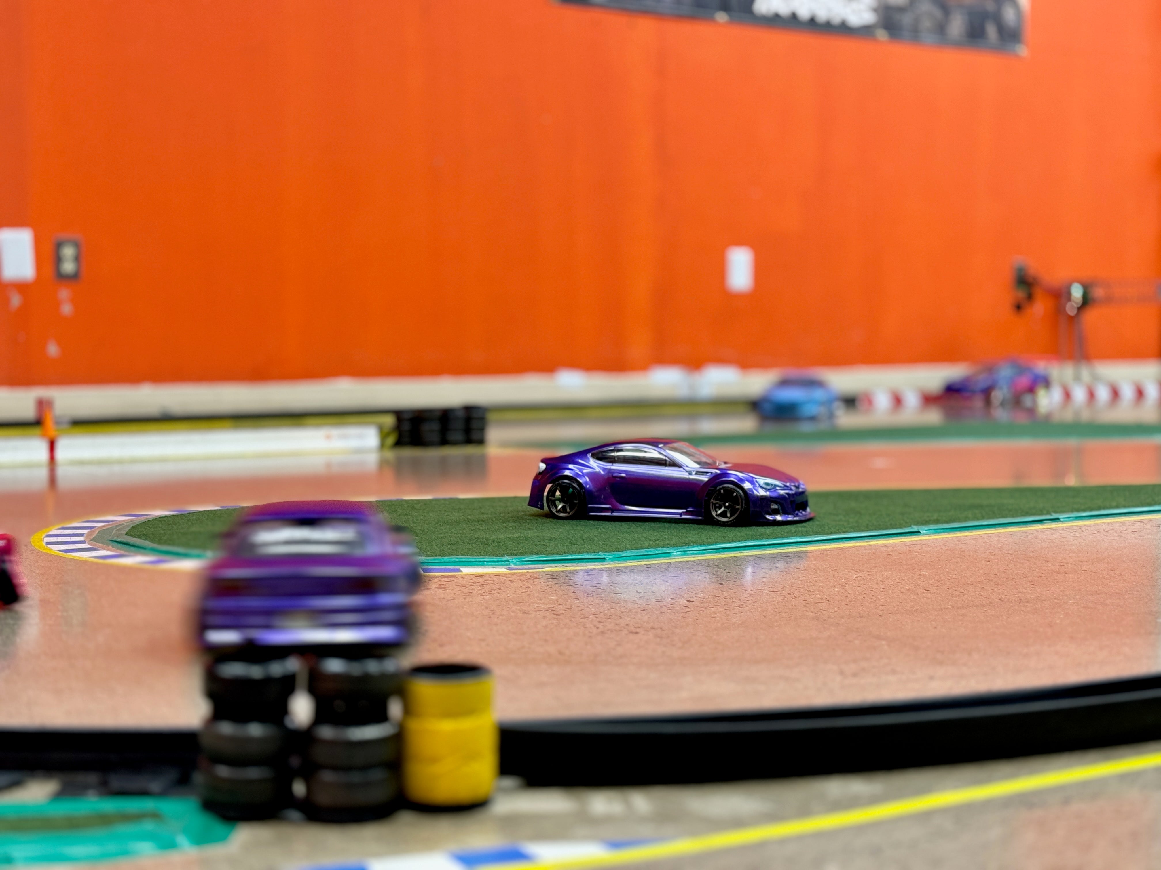 a drift car sits in the green space while a drift car slides around it on track